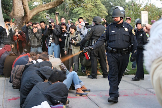 A police officer pepper sprays seated UC Davis students at an Occupy protest.